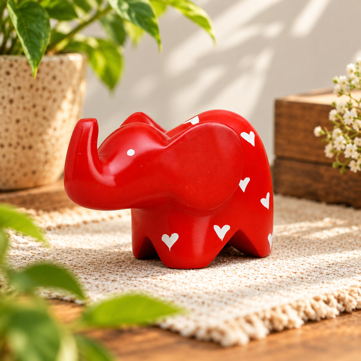 Red big-eared soapstone elephant with white hearts on a woven mat in a warm natural setting