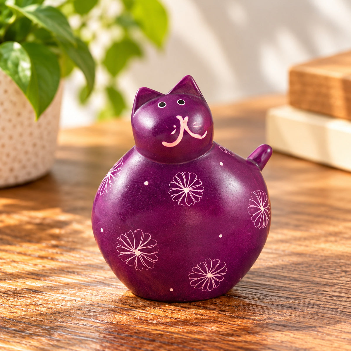 Purple handmade soapstone fat cat with floral patterns displayed on a wooden tabletop